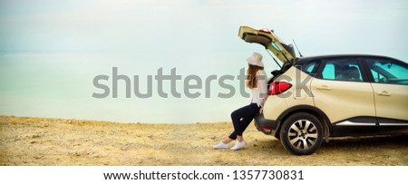 View of young woman traveler looking at sea sunset, sitting on hatchback car with the copy space. Banner.