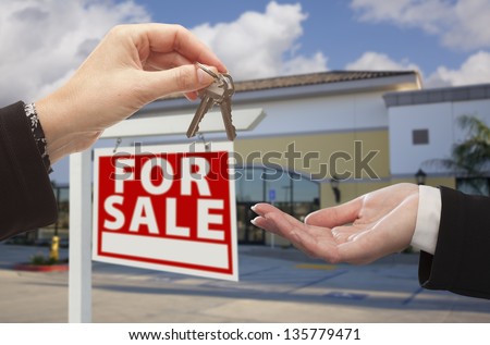 Real Estate Agent Handing Over the Keys in Front of Vacant Business Office and For Sale Sign.