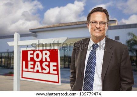 Handsome Businessman In Front of Vacant Office Building and For Lease Real Estate Sign.