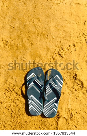 Summer slippers. Navy blue flip flop on yellow sand beach background. Copy space, top view. Holiday and travel concept.