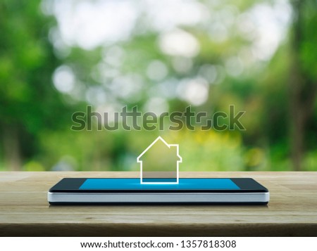 House icon with copy space on modern smart mobile phone screen on wooden table over blur green tree in park, Businesss real estate online concept
