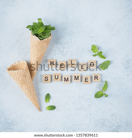 Ice cream waffle cone with mint leaves on blue background. Summer card. Wooden letters words Hello Summer. Top view, flat lay, square image