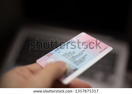 Person holds UK Residence Permit - BRP card in hand and computer in the background. Immigration concept image.  Royalty-Free Stock Photo #1357875317