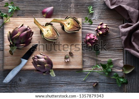 Flat lay with fresh red artishokes, whole and halved, on cutting board on rustic wooden background Royalty-Free Stock Photo #1357879343