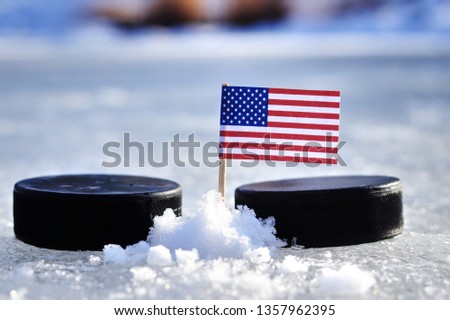 American flag on toothpick between two hockey pucks. Winter classic. Flag on frozen pond on unkempt ice. Traditional pucks for international matches.