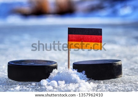 Germany flag on toothpick between two hockey pucks. Winter classic. Flag on frozen pond on unkempt ice. Traditional pucks for international matches