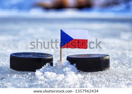 Czech flag on toothpick between two hockey pucks on ice in outdoor. Winter classic. Flag on frozen pond on unkempt ice. Old ice hockey style. Royalty-Free Stock Photo #1357962434
