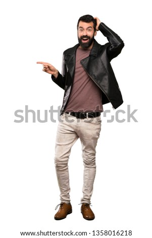 Handsome man with beard surprised and pointing finger to the side over isolated white background