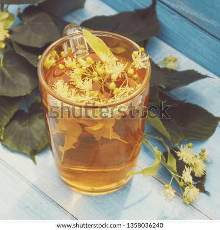 Tea with lime. Fragrant herbal tea with Linden on wooden table on background of branches of a Linden tree.
