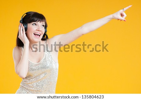 Carefree young woman listening to music and gesturing, yellow background
