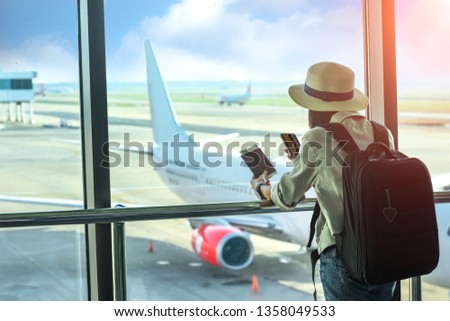 woman passenger or traveler tourist looking at next flight schedule on mobile, in worry of the flight schedule in late or delay, sitting upset in the transit hall of the airport waiting for aircraft Royalty-Free Stock Photo #1358049533