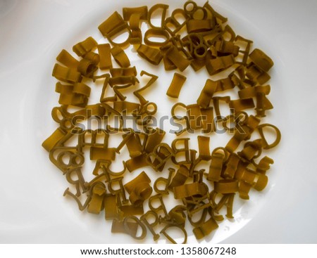 Corn macaroni with green spinach in the form of numbers and letters on a white plate in its raw solid form