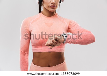 Picture of a beautiful young amazing strong sports fitness woman posing isolated over white wall background listening music with headphones looking at watch.