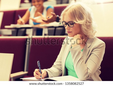 education, high school, university, learning and people concept - student girl writing to notebook in lecture hall