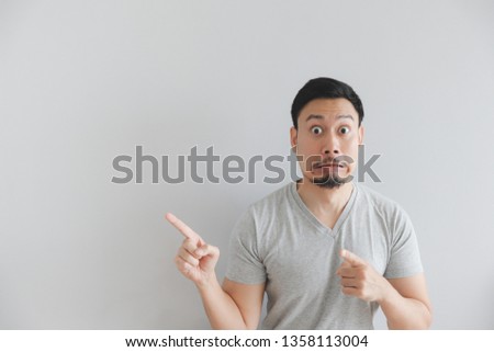 Shocked face of Asian man in grey t-shirt with hand point on empty space.