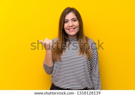 Young girl over yellow wall pointing to the side to present a product