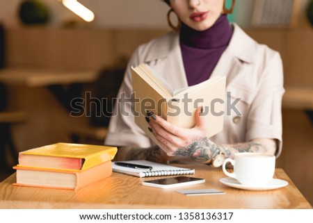 partial view of businesswoman holding book while sitting at table in cafe