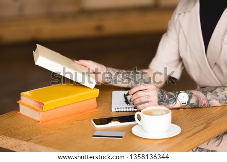 partial view of businesswoman sitting at table with books, smartphone and coffee cup 