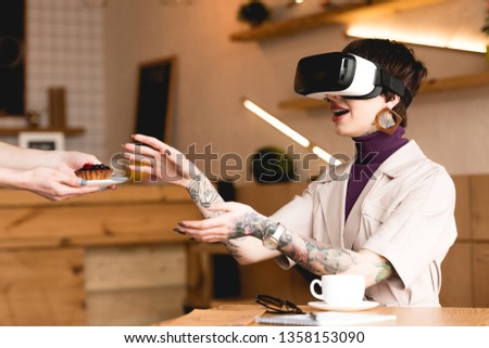 smiling businesswoman in virtual reality headset taking saucer with cake from waitress