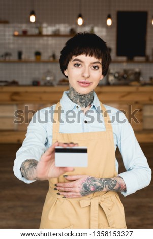smiling waitress proprietor in apron holding credit card and looking at camera