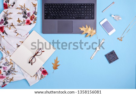 Home office workspace with laptop, glasses and dress on blue background. Fashion blogger work concept. Flat lay