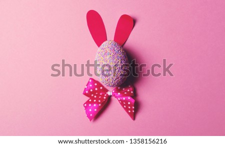 Easter bunny with shadow made of decorated egg with paper ears and dotted magenta bow on pink background. Easter holiday symbol and tradition concept. Flat lay.