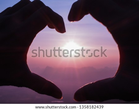 Silhouette hand between the sunrise, try to make heart shape