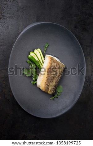 Fried Danish skrei cod fish filet with baby zucchini and lettuce as top view on a modern design plate 