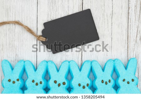 Blue candy bunnies with gift tag on weathered whitewash textured wood background with copy space for your Easter message