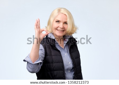 Smiling senior blonde lady gesturing ok sign