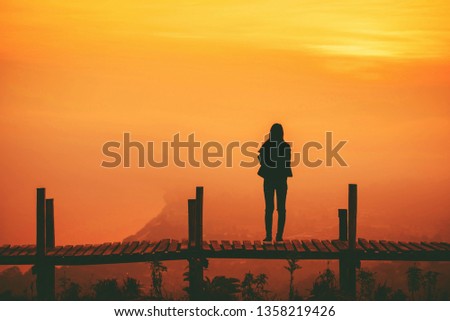 Silhouette woman standing on wooden bridge on hill mountain and sunset yellow sky background 