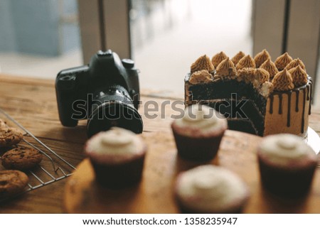 Digital camera on table with freshly made cakes, cookies and cupcakes on wooden table. Dslr camera with pastry items on a table.