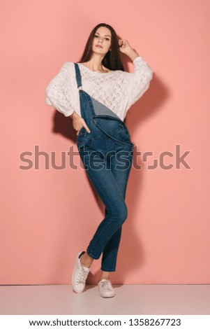brunette and beautiful woman in denim overalls with hand on hip looking at camera 