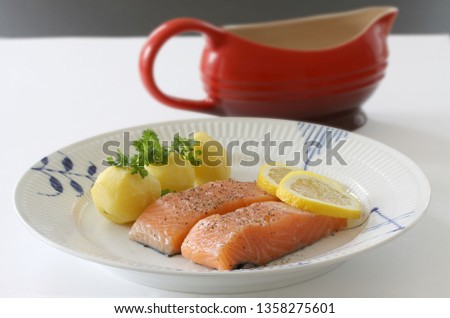 Salmon fillet with potatoes, lemon slices and parsley served on a plate. Close up stock photo.