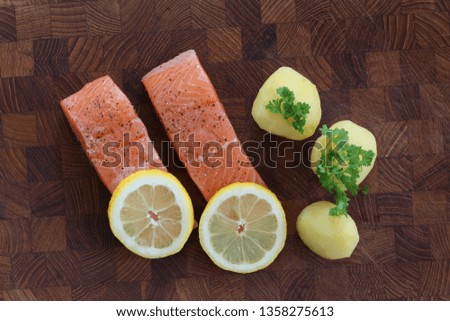 Salmon fillet with potatoes, lemon slices and parsley served on a wooden board. Top view close up stock photo.