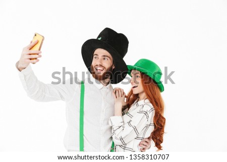 Happy young couple wearing costumes, celebrating St.Patrick 's Day isolated over white background, taking a selfie
