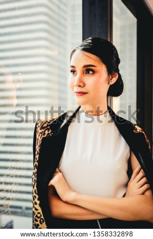 Successful business asian woman standing against glass window in modern office with buildings city background.
