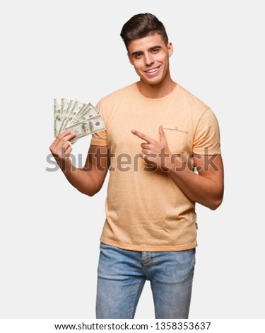 Young man holding dollars smiling and pointing to the side