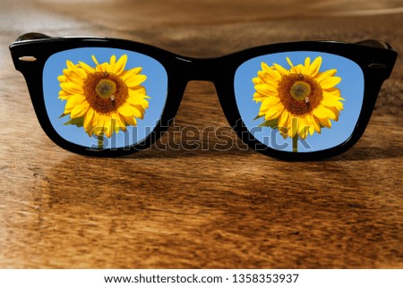Sunglasses on a Wooden Tabel Reflecting a Sunflower in Front of Blue Sky