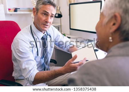 Front view of matured Caucasian male doctor and senior African American woman interacting with each other in clinic at retirement home
