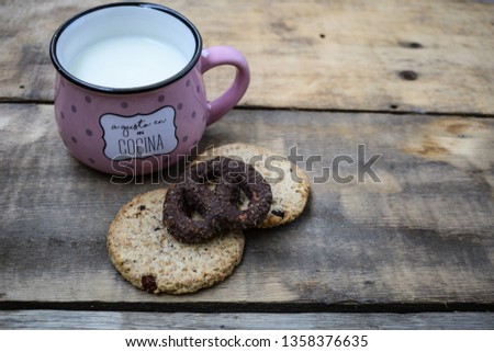 Oatmeal cookies and chocolate pretzel with cup of milk on a wooden background, close up. A gusto en mi cocina means: The taste of my kitchen 
