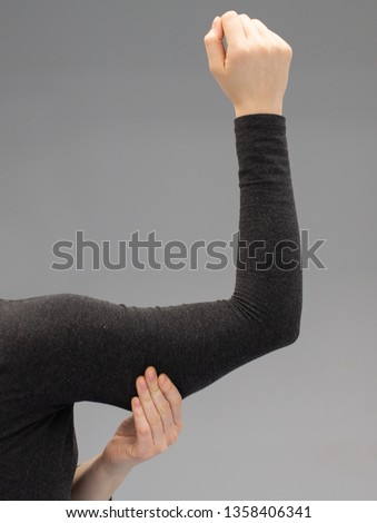A closeup view of a young Caucasian lady squeezing her upper arm, showing the sagging skin and fat beneath the triceps, commonly referred to as bingo wings. Royalty-Free Stock Photo #1358406341