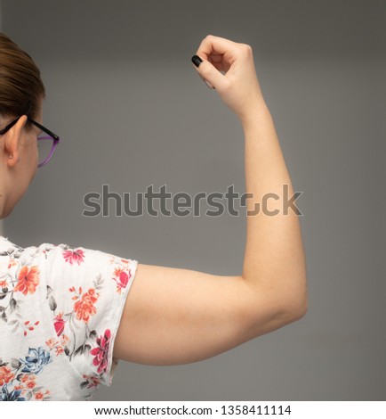 A closeup view of a Caucasian woman holding her arm in the air showing sagging skin beneath the triceps, commonly referred to as bingo wings. Royalty-Free Stock Photo #1358411114