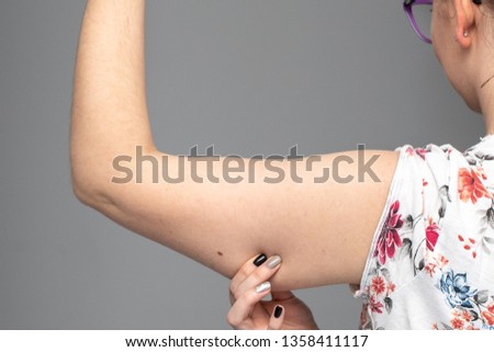 A closeup view of a Caucasian woman squeezing her arm showing saggy muscles and skin in her upper arm, commonly referred to as bingo wings. Royalty-Free Stock Photo #1358411117