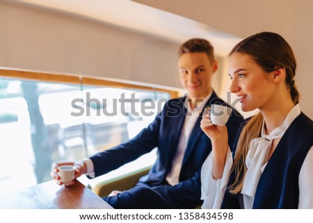 A stylish couple drinks morning coffee at the cafe with cozy interior, young businessmen and freelancers