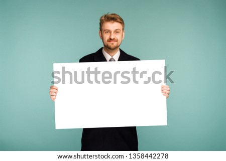 Happy smiling young business man showing blank signboard, on blue background