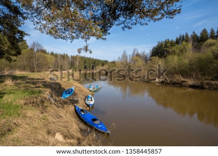 Five kayaks are located near the river Bank. Sunny landscape with forest, pine trees and blue sky. A narrow river with brown water. Spring in Russia