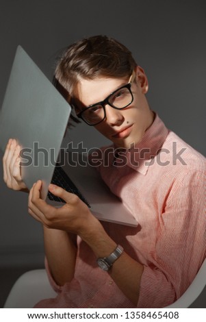 IT computer nerd. Creative teen millenial portrait indoors. Funny young man with happy face expression in glasses hug laptop against dark background. Internet, video game addiction concept