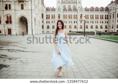 The girl runs and laughs near a beautiful building at sunset