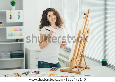 The cute woman with an art brush painting a picture on the easel